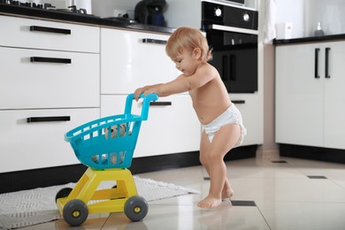 Photo of Cute baby with toy walker in kitchen. Learning to walk