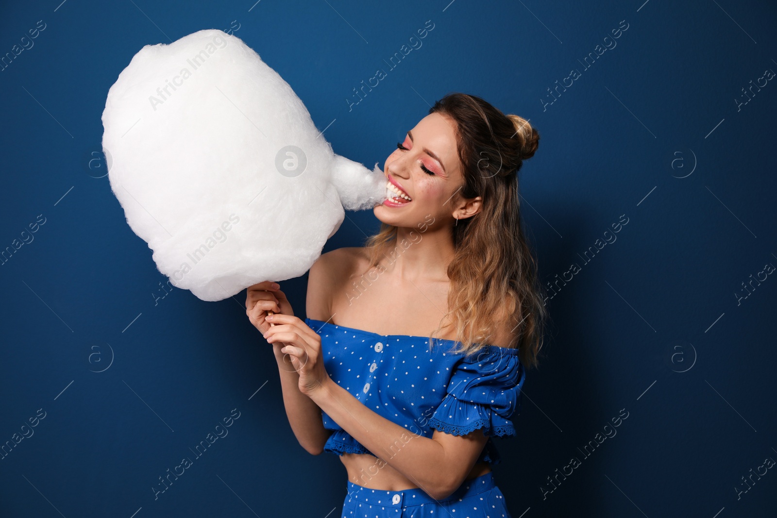 Photo of Portrait of young woman biting cotton candy on blue background