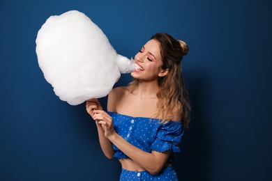 Portrait of young woman biting cotton candy on blue background
