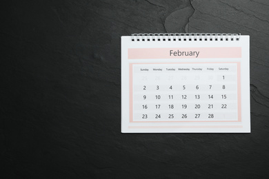 Photo of February calendar on black stone background, top view. Space for text