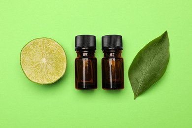 Bottles of citrus essential oil, fresh lime and leaf on green background, flat lay