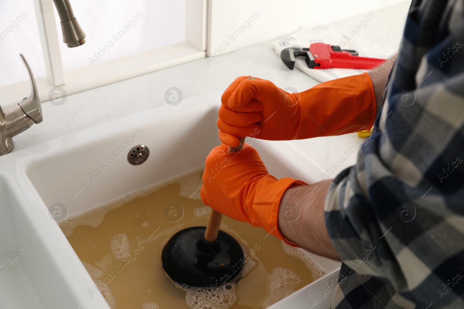 Photo of Man using plunger to unclog sink drain in kitchen, closeup