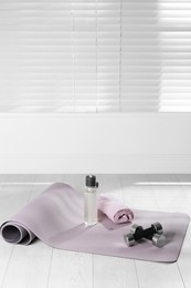 Photo of Exercise mat, dumbbells, towel and bottle of water on light wooden floor indoors