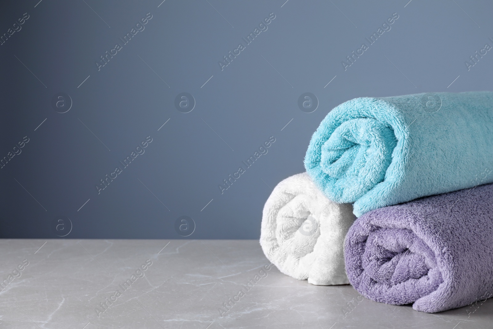 Photo of Fresh rolled bath towels on grey table. Space for text