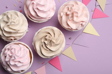 Photo of Delicious birthday cupcakes, sprinkles and bunting flags on violet background, flat lay