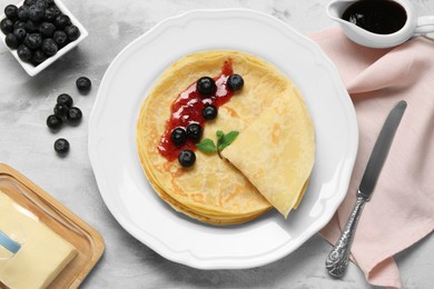 Photo of Delicious crepes with blueberries, mint and jam on light grey table, flat lay