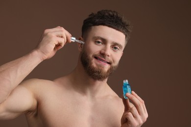 Photo of Handsome man applying serum onto his face on brown background