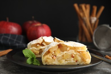 Photo of Delicious apple strudel with almonds, powdered sugar and mint on grey table