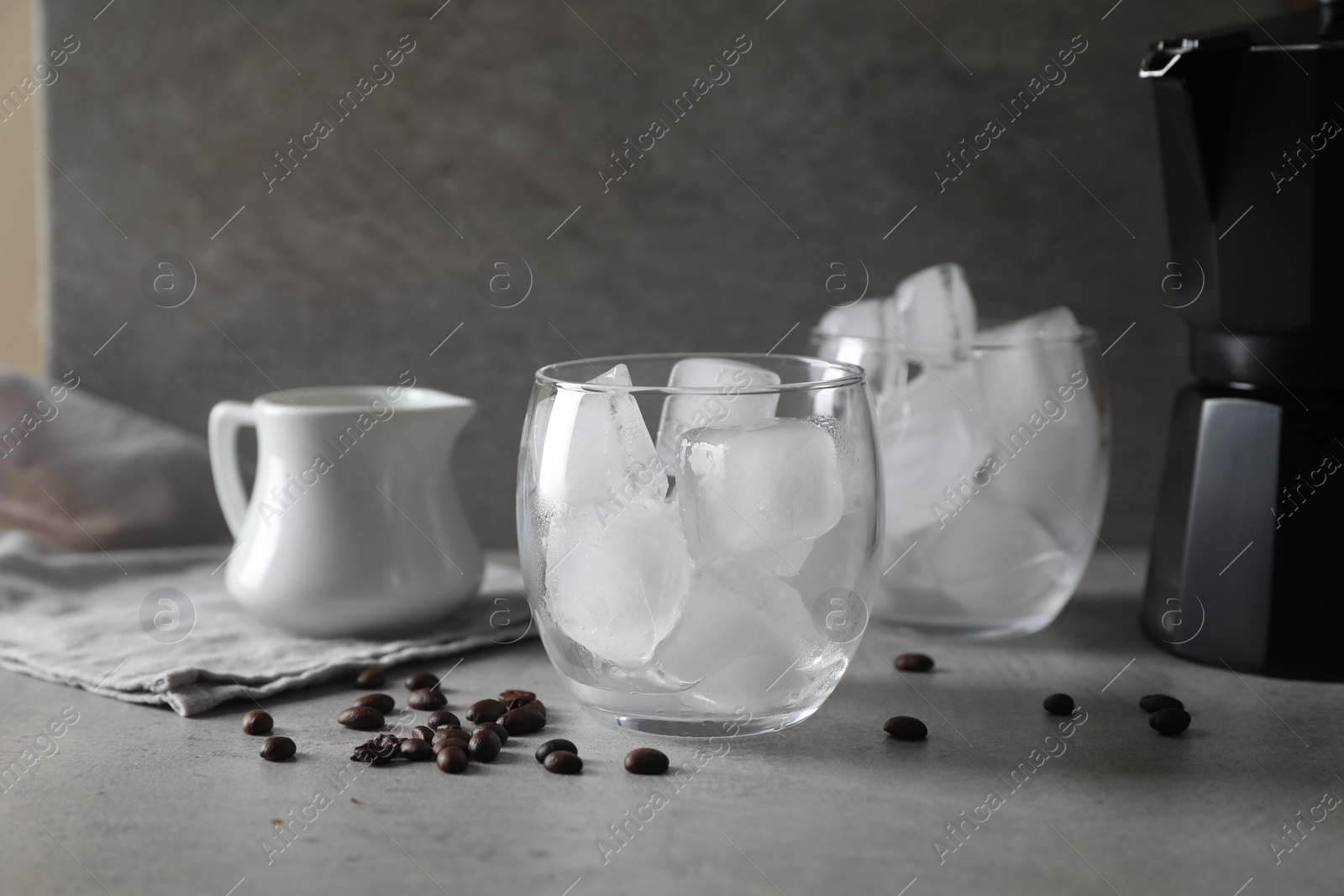 Photo of Making iced coffee. Ice cubes in glasses and ingredients on gray table, closeup