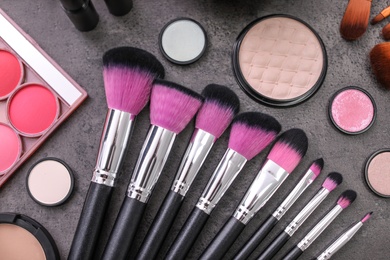 Makeup products and brushes on grey background