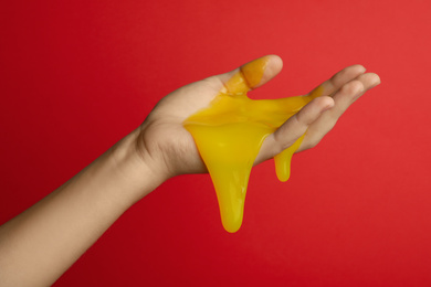 Photo of Woman playing with yellow slime on red background, closeup. Antistress toy