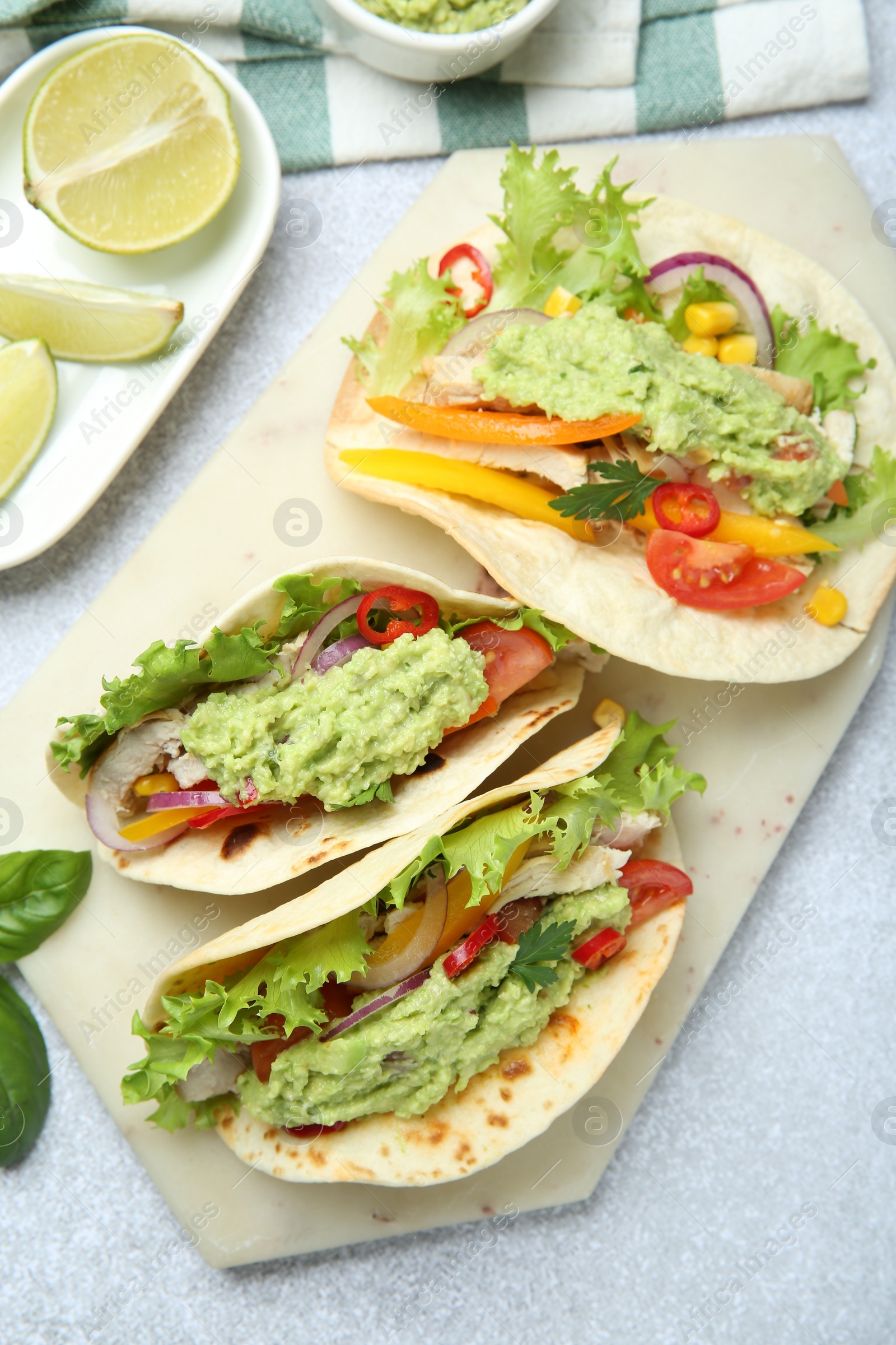 Photo of Delicious tacos with guacamole, meat and vegetables on light grey table, flat lay