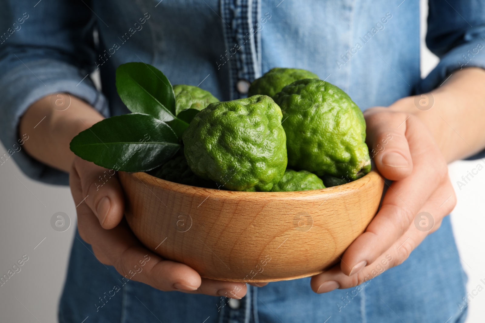 Photo of Woman holding wooden bowl with fresh ripe bergamot fruits on white background, closeup