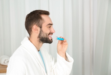 Young man using teeth whitening device at home. Space for text