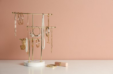 Photo of Holder with set of luxurious jewelry and lipstick on white table near pale pink wall, space for text