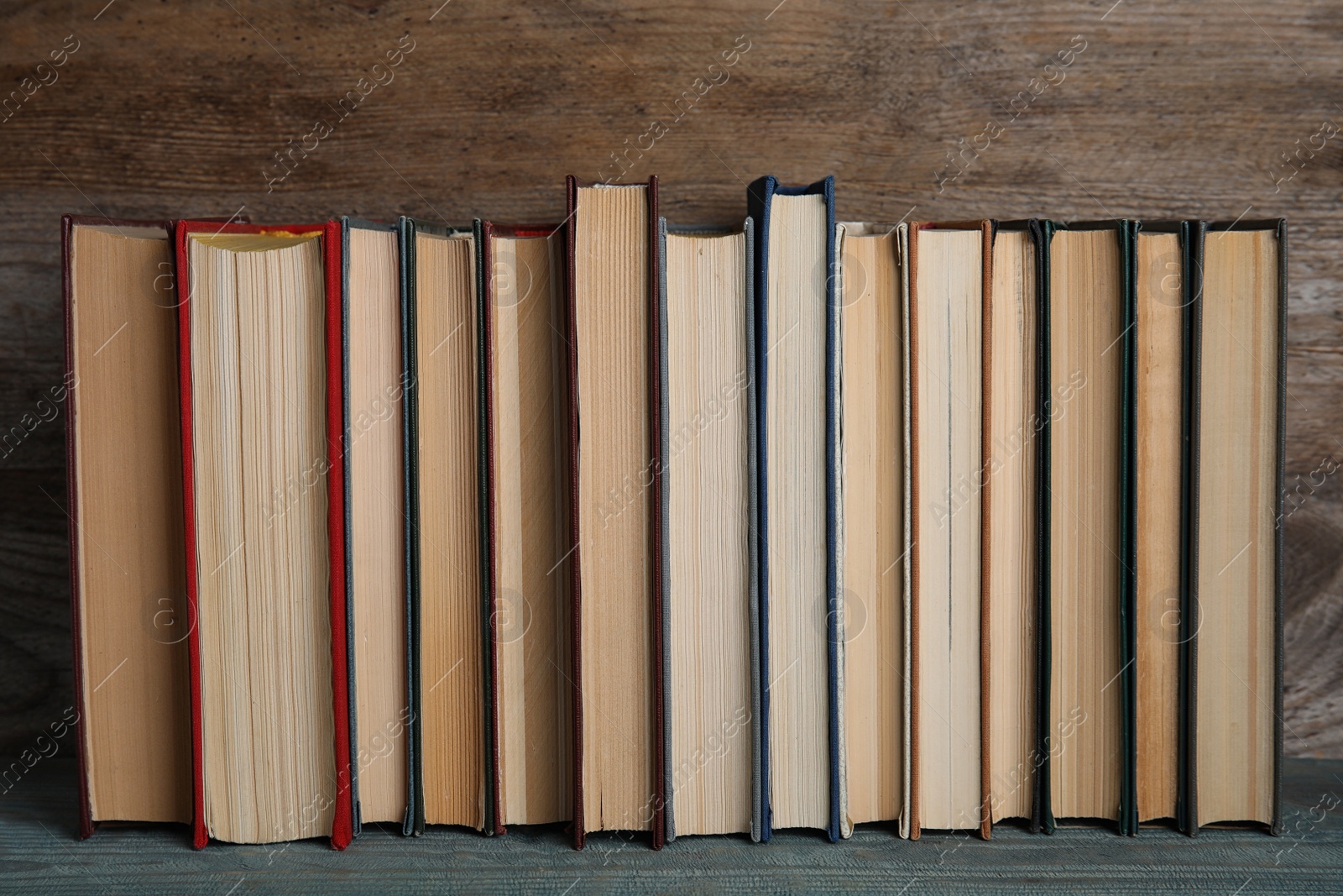 Photo of Stack of hardcover books on light blue table against wooden background