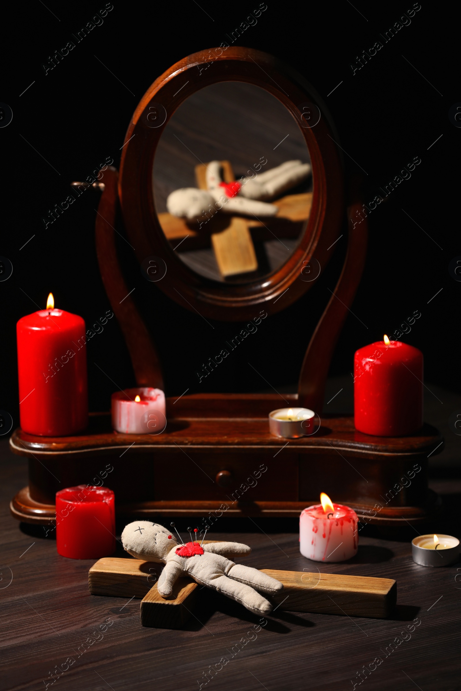 Photo of Voodoo doll with pins in heart and ceremonial items on wooden table