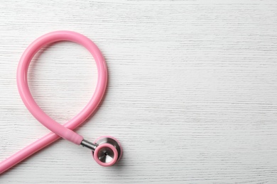 Photo of Pink stethoscope folded like awareness ribbon on wooden background, top view with space for text. Breast cancer concept