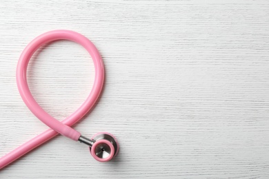 Pink stethoscope folded like awareness ribbon on wooden background, top view with space for text. Breast cancer concept