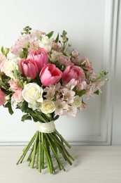 Photo of Beautiful bouquet of fresh flowers on table near white wall