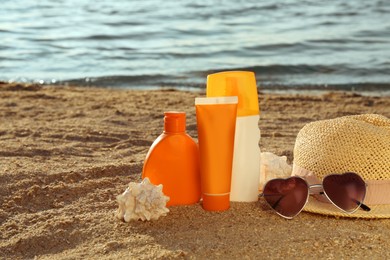 Sun protection products and beach accessories on sand near sea, space for text