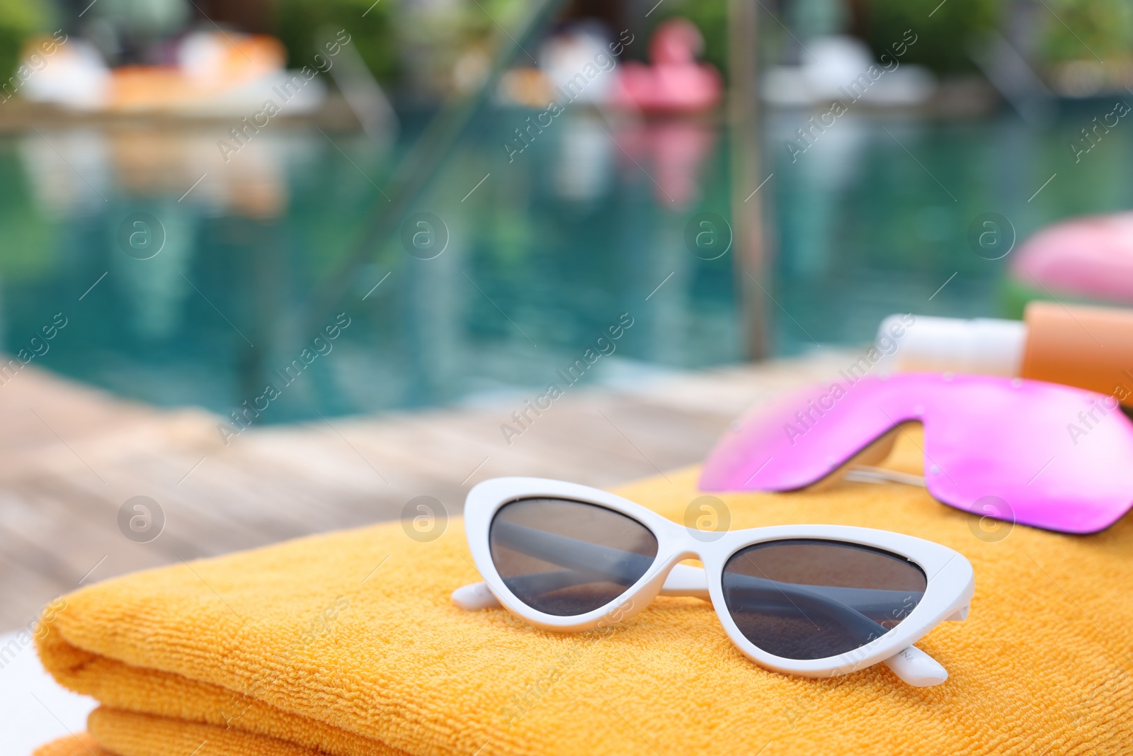 Photo of Beach towel and sunglasses near outdoor swimming pool at luxury resort, closeup. Space for text