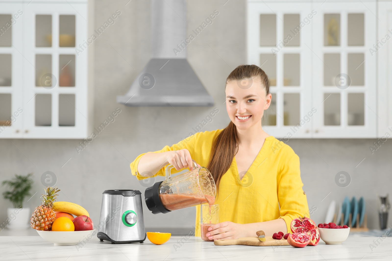 Photo of Woman pouring tasty smoothie into glass at white table in kitchen