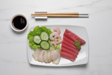 Photo of Sashimi set (raw slices of tuna, oily fish and shrimps) served with cucumber, lettuce, vasabi and soy sauce on white marble table, flat lay