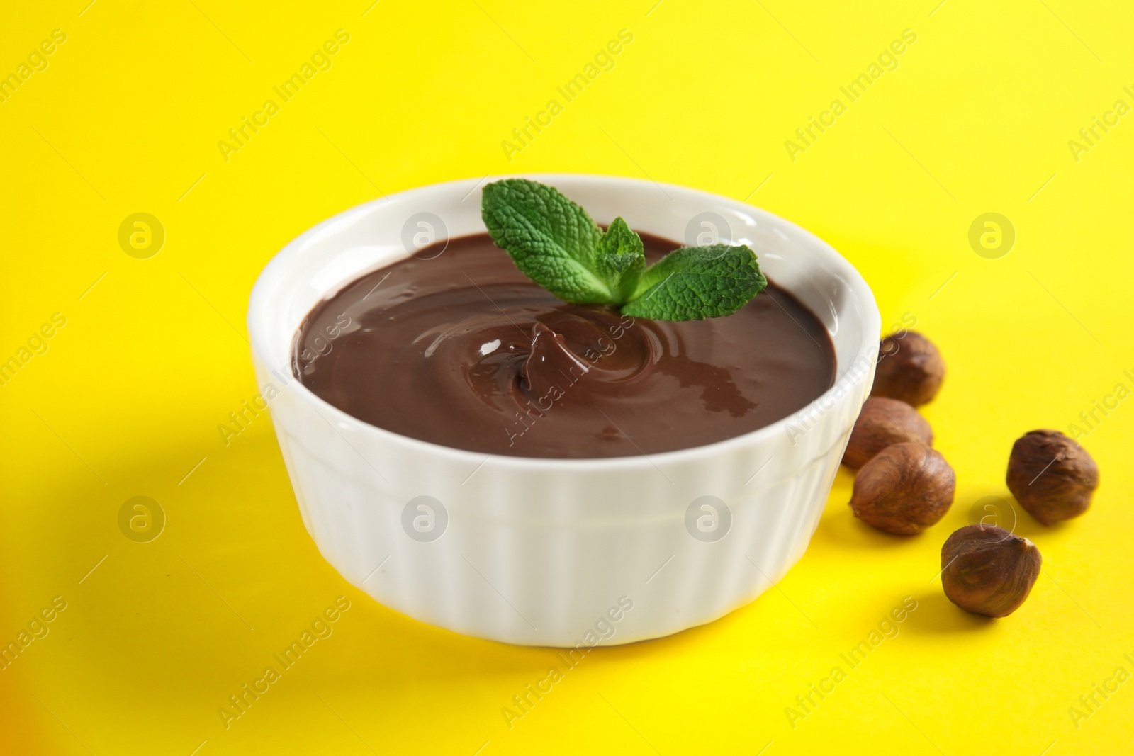 Photo of Ceramic bowl with sweet chocolate cream, hazelnuts and mint on color background