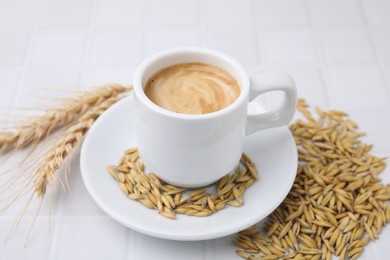 Cup of barley coffee, grains and spikes on white table, closeup