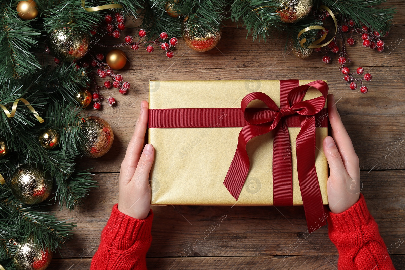 Photo of Christmas present. Woman with gift box and decorated fir tree branches at wooden table, top view