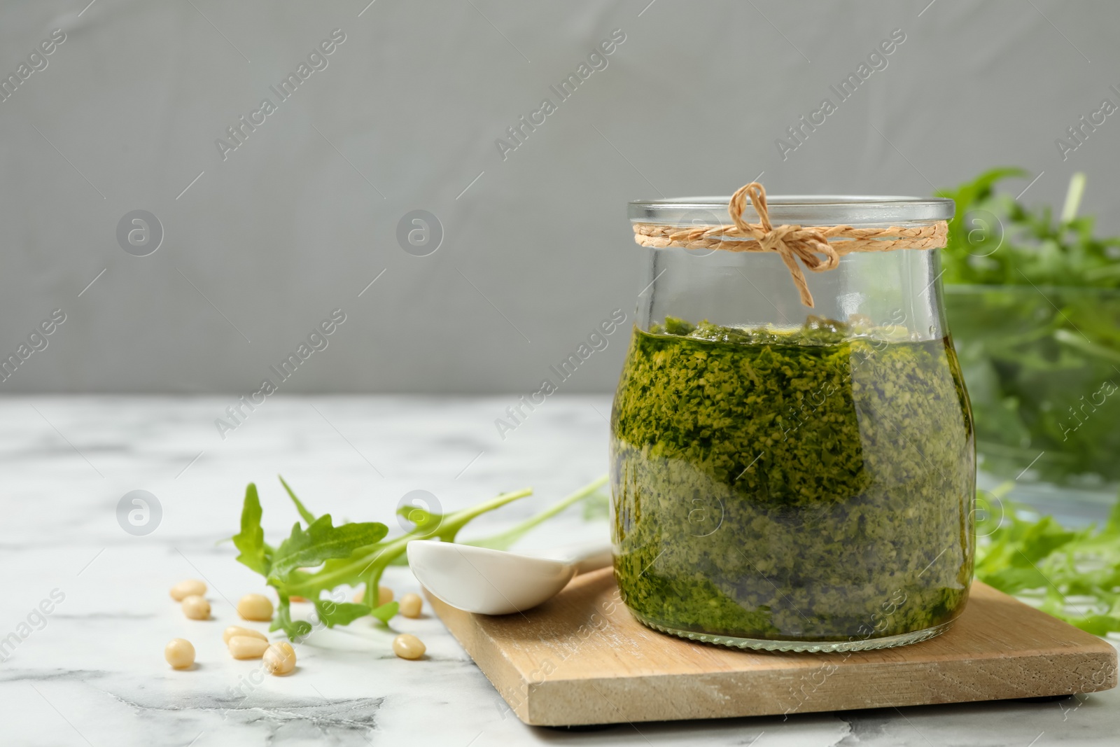 Photo of Jar of tasty arugula pesto and ingredients on white marble table