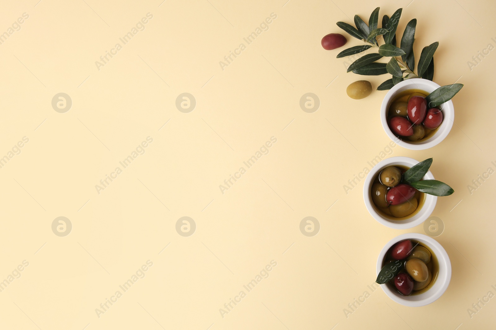 Photo of Bowls with different ripe olives and leaves on beige background, flat lay. Space for text