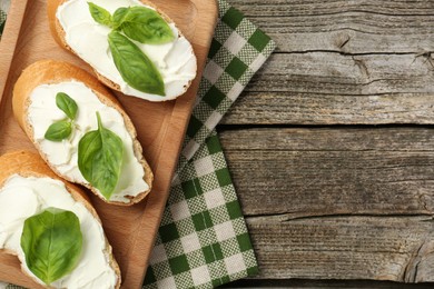 Photo of Delicious sandwiches with cream cheese and basil leaves on wooden table, top view. Space for text