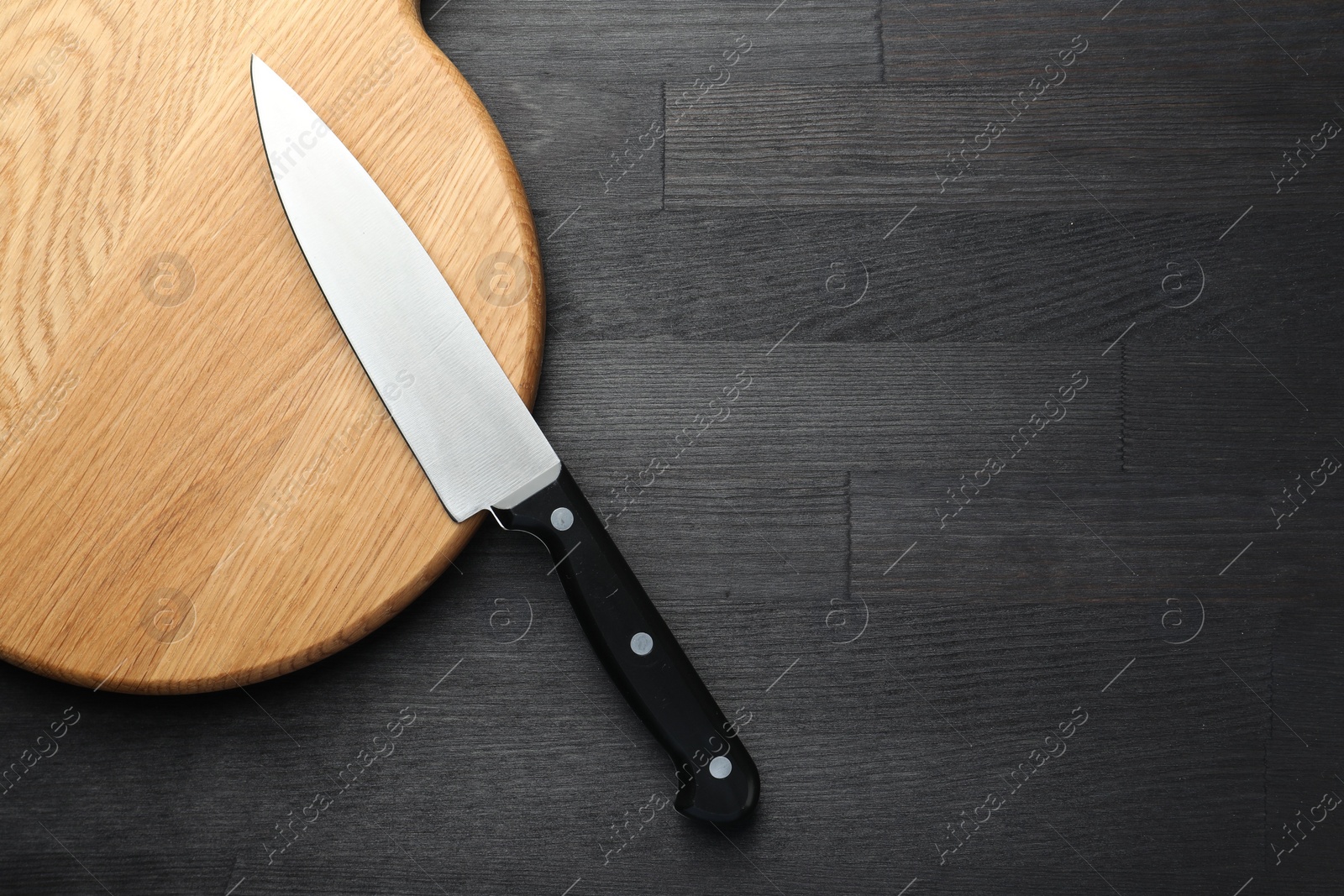 Photo of One sharp knife and board on black wooden table, top view. Space for text