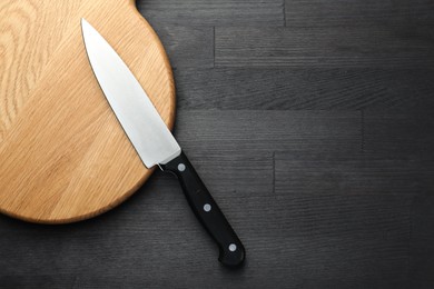 Photo of One sharp knife and board on black wooden table, top view. Space for text