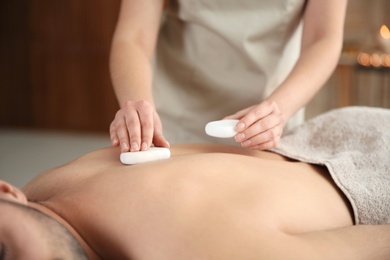 Photo of Man receiving hot stone massage in spa salon, closeup