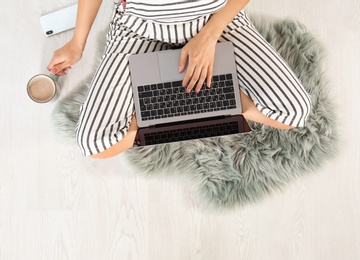 Young woman with cup of coffee and laptop sitting on floor, top view