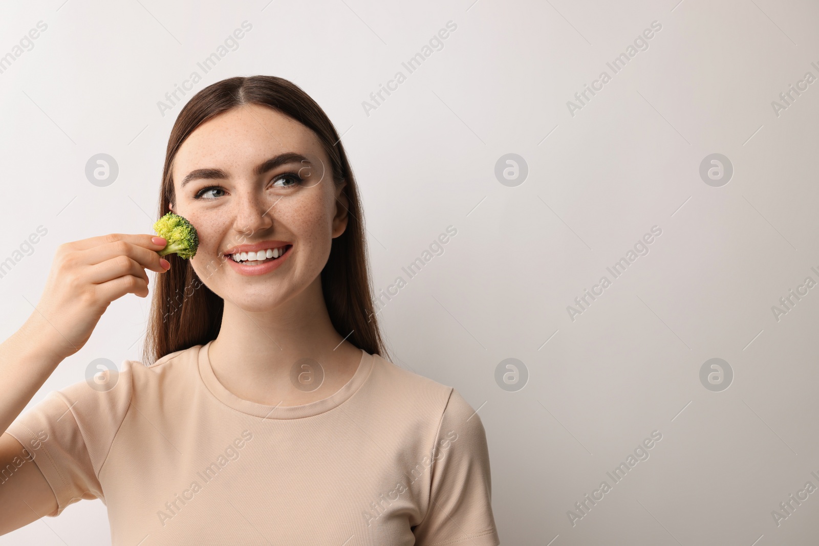 Photo of Smiling woman making fake freckles with broccoli and cosmetic product on light background. Space for text