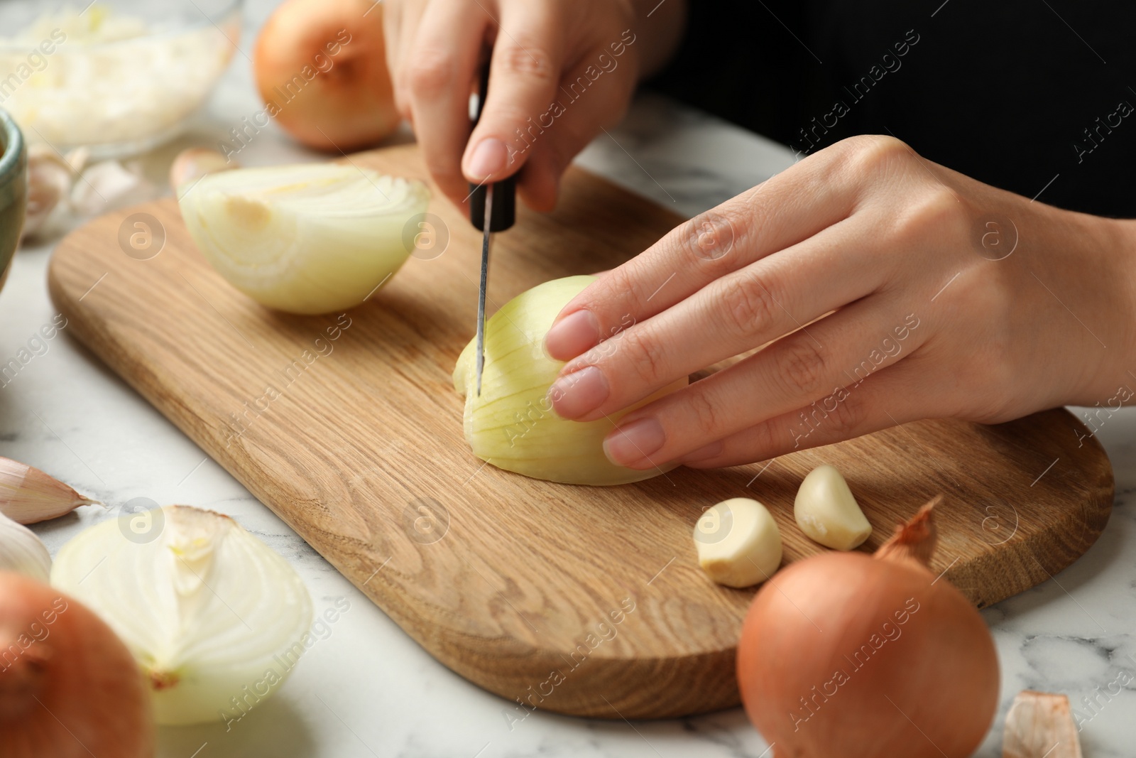 Photo of Woman cutting fresh onion on wooden board, closeup