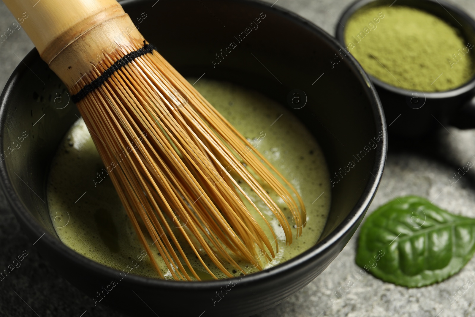 Photo of Cup of fresh green matcha tea with bamboo whisk on grey table, closeup