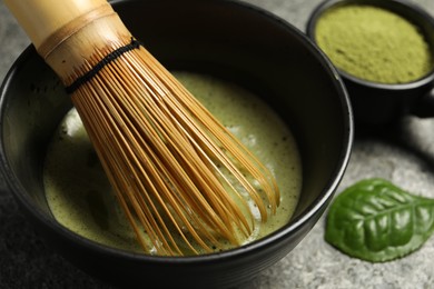 Photo of Cup of fresh green matcha tea with bamboo whisk on grey table, closeup