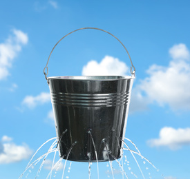 Image of Leaky bucket with water against blue sky