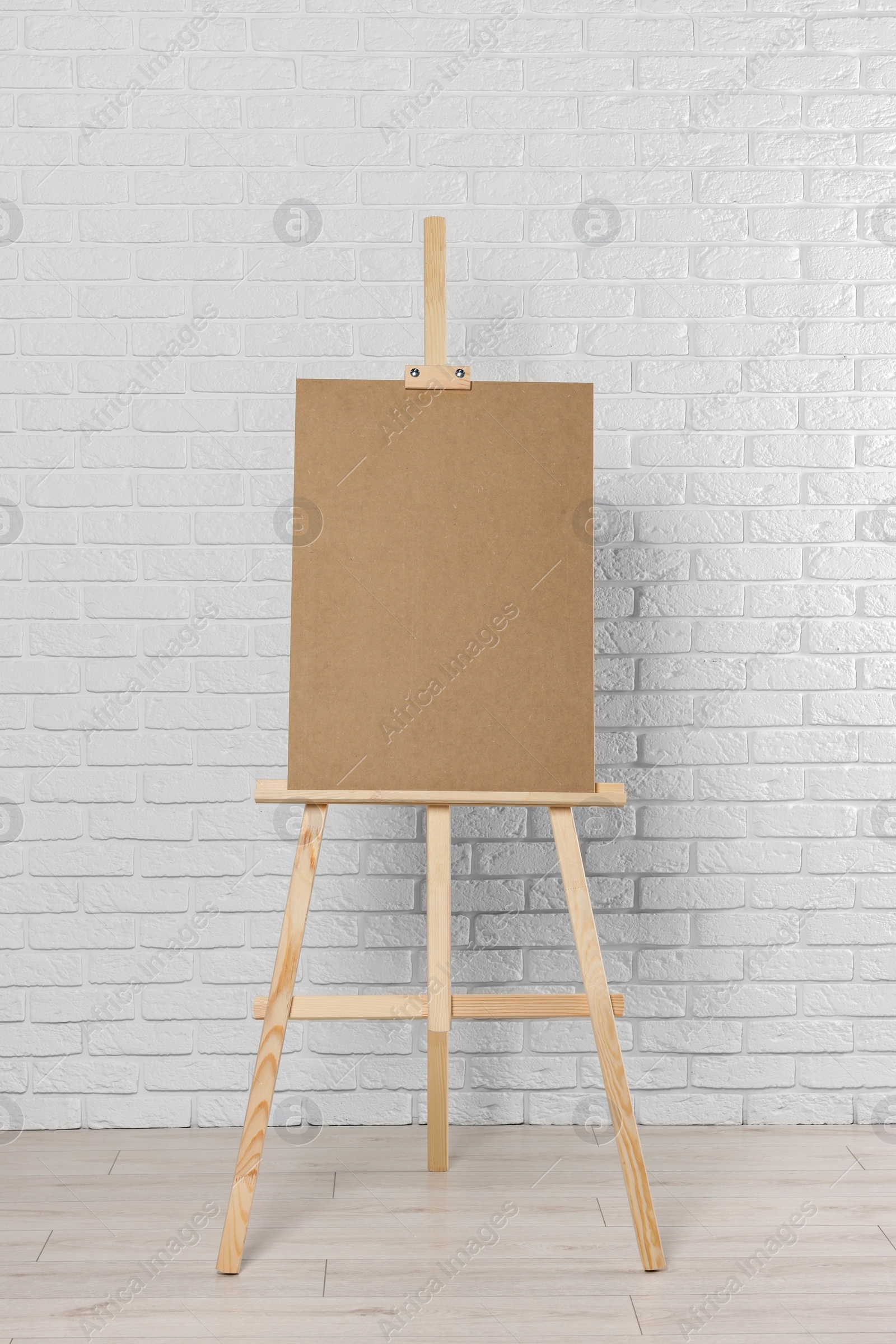 Photo of Wooden easel with blank board near white brick wall indoors