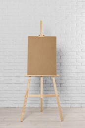 Wooden easel with blank board near white brick wall indoors