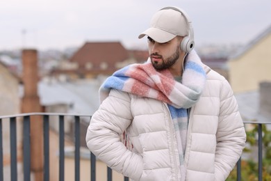 Photo of Handsome man in warm scarf and headphones outdoors