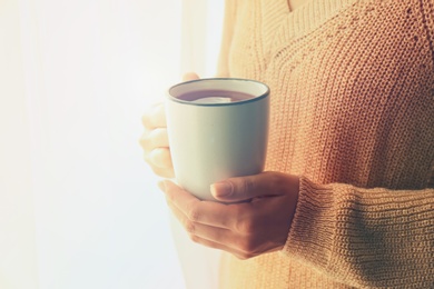 Photo of Woman holding elegant cup with tea near window indoors, closeup