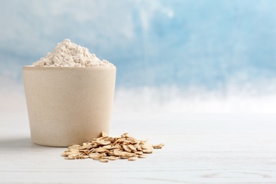 Photo of Bowl with oat flour and flakes on table against color background. Space for text