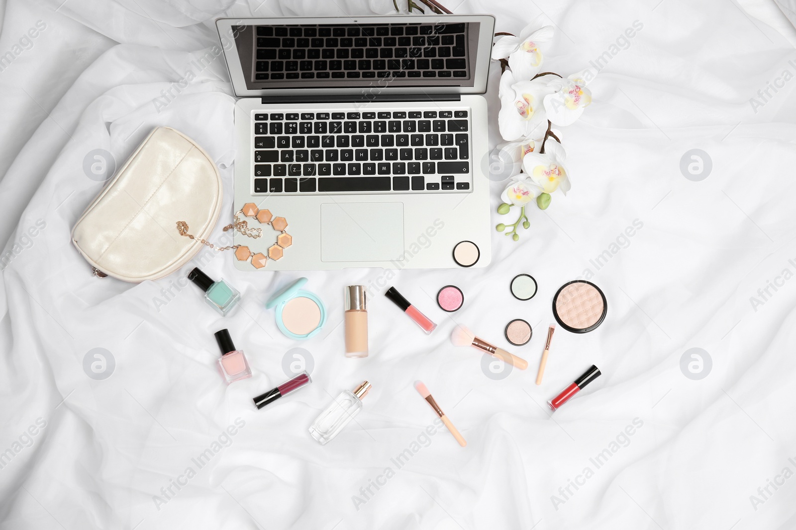 Photo of Flat lay composition with laptop and makeup products for woman on bed