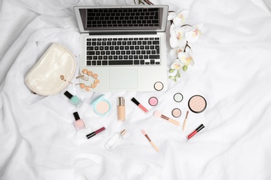 Photo of Flat lay composition with laptop and makeup products for woman on bed